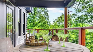 Een houten terras met een ronde tafel, groen glaswerk, rieten manden en uitzicht op weelderige begroeiing.