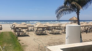 Um resort à beira-mar com várias cabanas de palha, cada uma equipada com mesas e cadeiras.