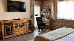 A bedroom with a bed, a wooden cabinet, a television, a rocking chair, a bookshelf, and a window with curtains. - Mid-Century Mountain Home with Breathtaking Views (Mill Valley)