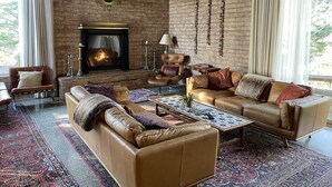 A cozy living room with leather sofas, a fireplace, and a brick wall. - Mid-Century Mountain Home with Breathtaking Views (Mill Valley)