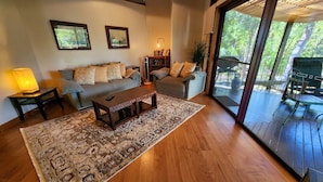 A living room with a sofa, coffee table, and a rug. There is a bookshelf and a lamp. The room has large windows and a view of greenery outside. - Sapphire Villa 535, Kingfisher Bay Resort, K'gari (Fraser Island)