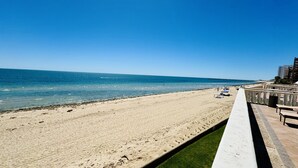 En strand med krystalklart hav, en sti langs kysten og en bygning med balkon.