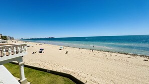 Ein Strand mit blauem Himmel, sandigem Ufer und einigen Sonnenschirmen.