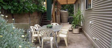 Un patio con mesa y sillas, rodeado de plantas en macetas y una pérgola de madera.