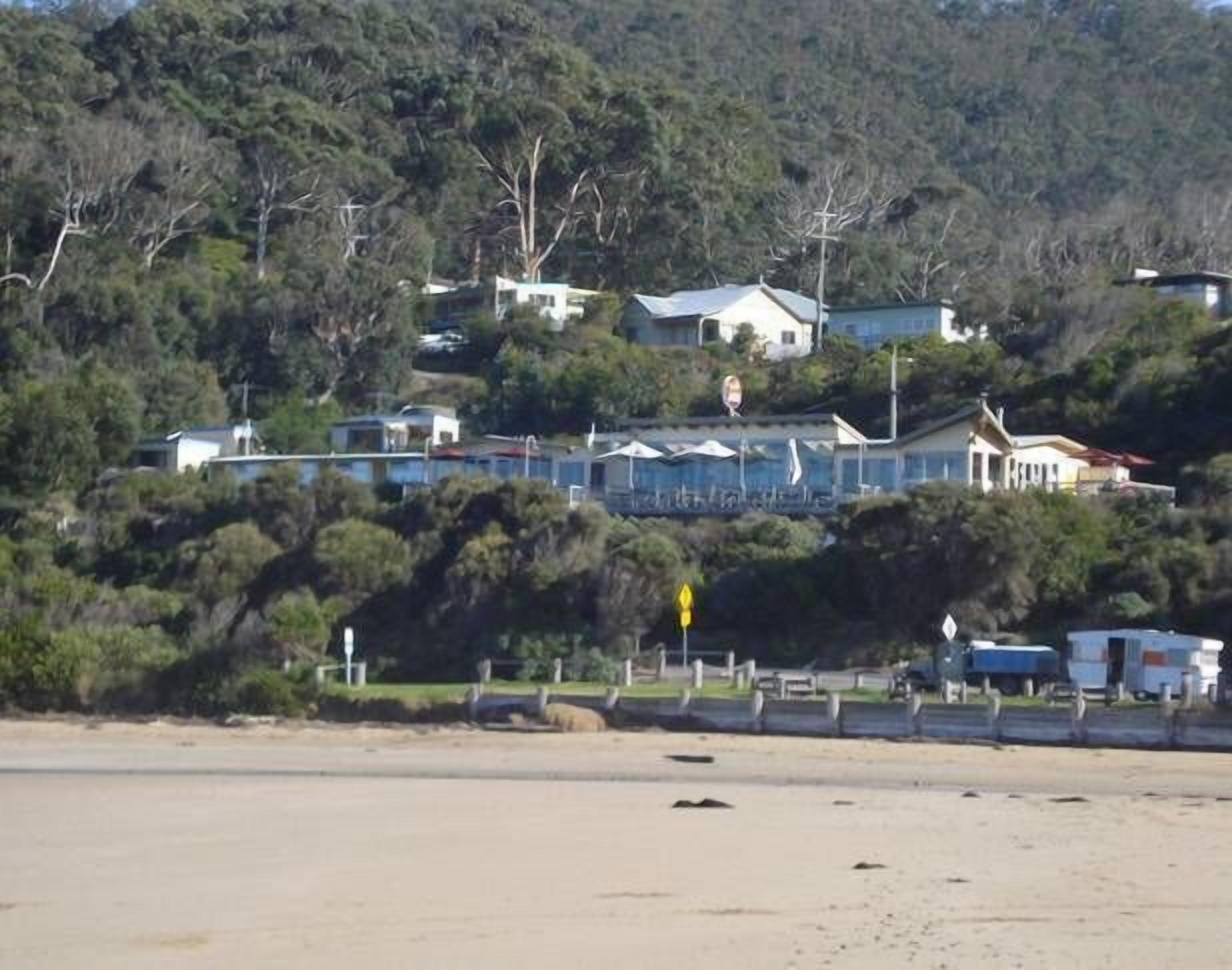 Uma área costeira com casas numa encosta, uma estrada e uma praia.