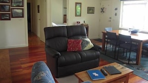 En stue med en sort lædersofa, et træbord og et spiseområde med bord og stole.