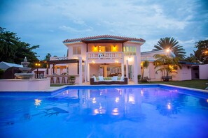 Una casa grande con piscina, un patio cubierto y un césped bien cuidado.