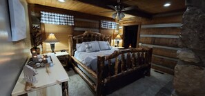 A cozy log cabin bedroom with a wooden bed, a desk with a lamp, and a stone wall. - Honeymoon Cabin, Very Secluded, Very Romantic, Arcade, FREE Daily Bear Sightings (Gatlinburg)