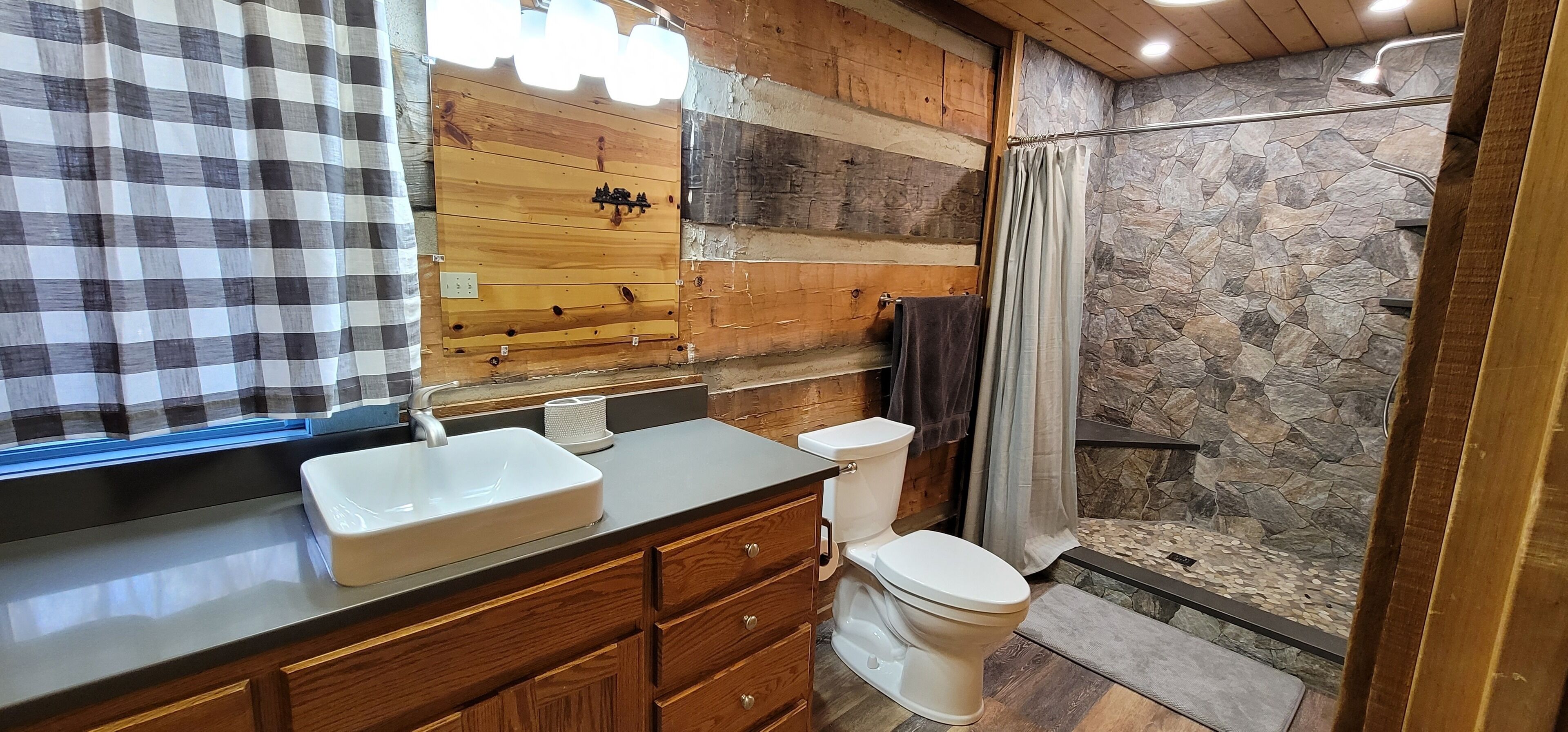 Een badkamer met een houten wastafelmeubel, een witte wastafel, toilet en douche met een achtergrond van een stenen muur.