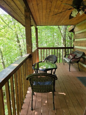 A wooden deck with wicker furniture and a glass table, overlooking a forested area. - Honeymoon Cabin, Very Secluded, Very Romantic, Arcade, FREE Daily Bear Sightings (Gatlinburg)