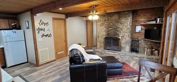 Un salon chaleureux avec une cheminée en pierre, un canapé en cuir noir et un plafond en bois.