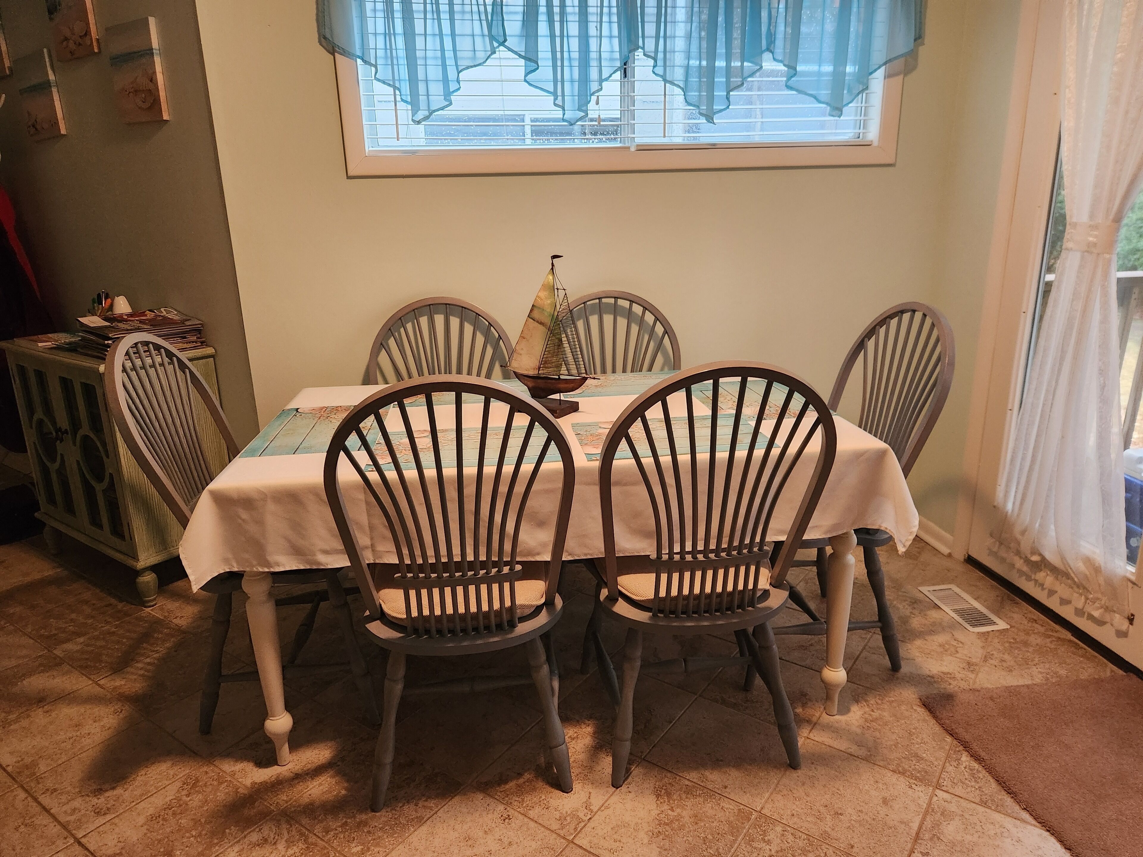 A dining area with a table set for four, surrounded by wooden chairs with cushioned seats. A decorative sailboat model is placed on the table.