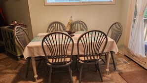 Un coin repas avec une table dressée pour quatre personnes, entourée de chaises en bois dotées d’assises rembourrées. Un modèle de voilier décoratif est posé sur la table.