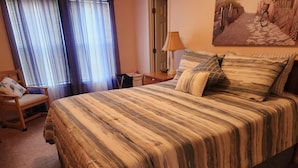 Un lit bien fait, avec une literie à rayures, une chaise avec un coussin, une lampe et un tableau accroché au mur.
