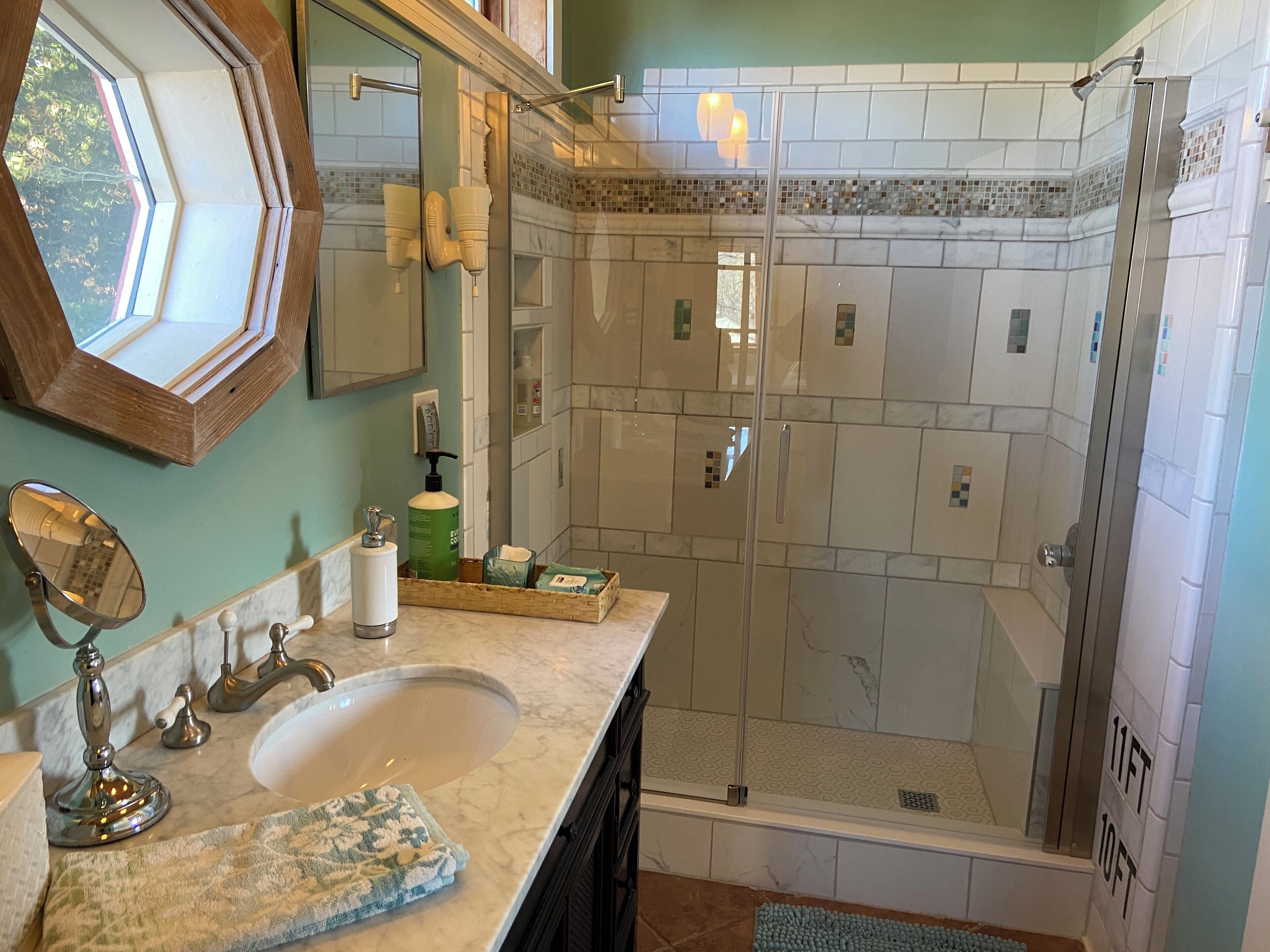 Une salle de bain dotée d’une douche à parois de verre, d’un lavabo avec un plan de travail en marbre et d’un miroir encadré en bois.