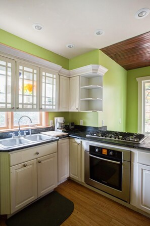 Uma cozinha com armários brancos, fogão preto e janela com vista para o verde.