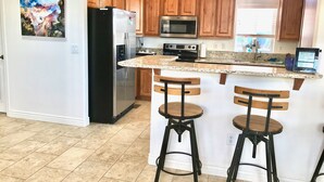A kitchen with wooden cabinets, a stainless steel refrigerator, a microwave, a stove, and a bar area with stools. - 🏜️Local VIEW~🐶Pet Friendly-🚤BOAT Parking~Close to AntelopeCanyon~HorseshoeBnd (Page)