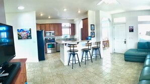 A modern kitchen with a central island, bar stools, and a dining area with a blue sofa and a lamp. - 🏜️Local VIEW~🐶Pet Friendly-🚤BOAT Parking~Close to AntelopeCanyon~HorseshoeBnd (Page)
