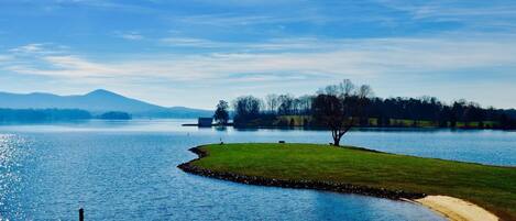 A lakeside view with a dock, grassy areas, and distant mountains.
