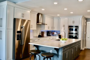 A modern kitchen with stainless steel appliances, white cabinetry, and a large island with stools. - Lake front, kayaks, SUP, WiFi, Views, pools,resort,beaches,docks (Moneta)