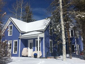 Ein zweistöckiges blaues Haus mit verschneitem Dach und Veranda.
