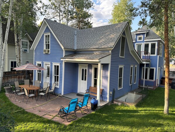 Ein zweistöckiges Haus mit überdachter Terrasse, einem Esstisch und Sitzgelegenheiten im Freien.