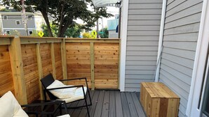 Une terrasse en bois avec deux chaises blanches dotées de coussins et un banc en bois.