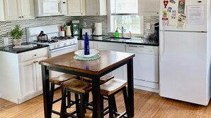 Una cucina con mobili bianchi, soffitto in legno, frigorifero bianco e un tavolo da pranzo con sgabelli.