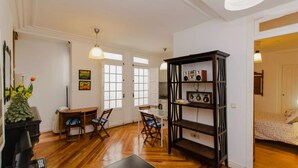 Una habitación con piso de madera, una mesa de comedor con sillas, una estantería y una cama.