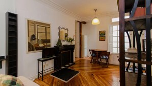 Una sala de estar con chimenea, una mesa de comedor con sillas, un mueble negro para televisión y un espejo grande en la pared.