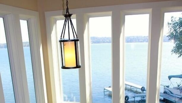 Una stanza con ampie finestre che danno su un corpo d'acqua, un lampadario, un divano e un tavolino con un vaso.