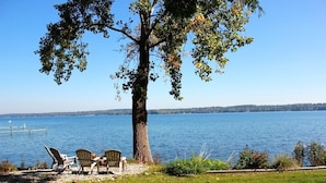 Vista sul lago con un grande albero, un pontile e due poltrone Adirondack.