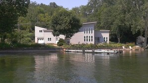 Una casa a due piani con un molo che si protende su un lago, circondata da alberi.