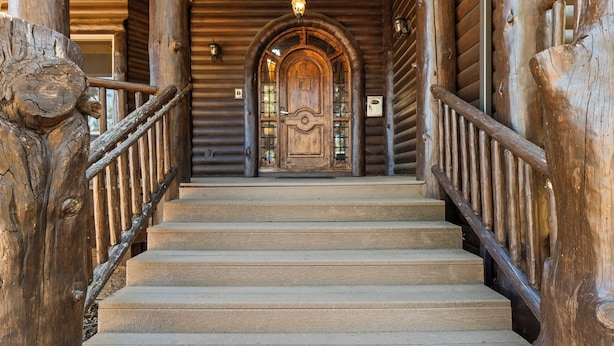 Un escalier en bois mène à une grande porte en arc de cercle, flanquée de rampes métalliques de chaque côté.