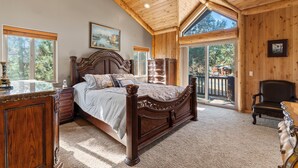 Une chambre spacieuse avec un grand lit, un plafond en bois et un balcon offrant une vue sur les arbres.