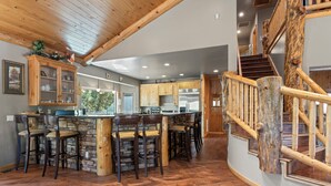 Une cuisine dotée d’un îlot central, de tabourets de bar en bois et d’un mur d’accent en pierre.