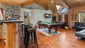 Une pièce spacieuse équipée d’une table de billard, d’un coin bar avec des tabourets, d’un canapé en cuir et d’une cheminée en pierre.