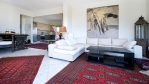 Un salon moderne avec un canapé d’angle blanc, un meuble de rangement noir pour appareils électroniques et un tapis rouge à motifs.