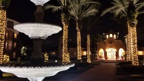 A night scene with a multi-tiered fountain, palm trees, and a building with lights in the background. - Presidential Suite 2100 sq-ft,  4  Bedroom  setup, Disney/Universal/Sea IS (Orlando)