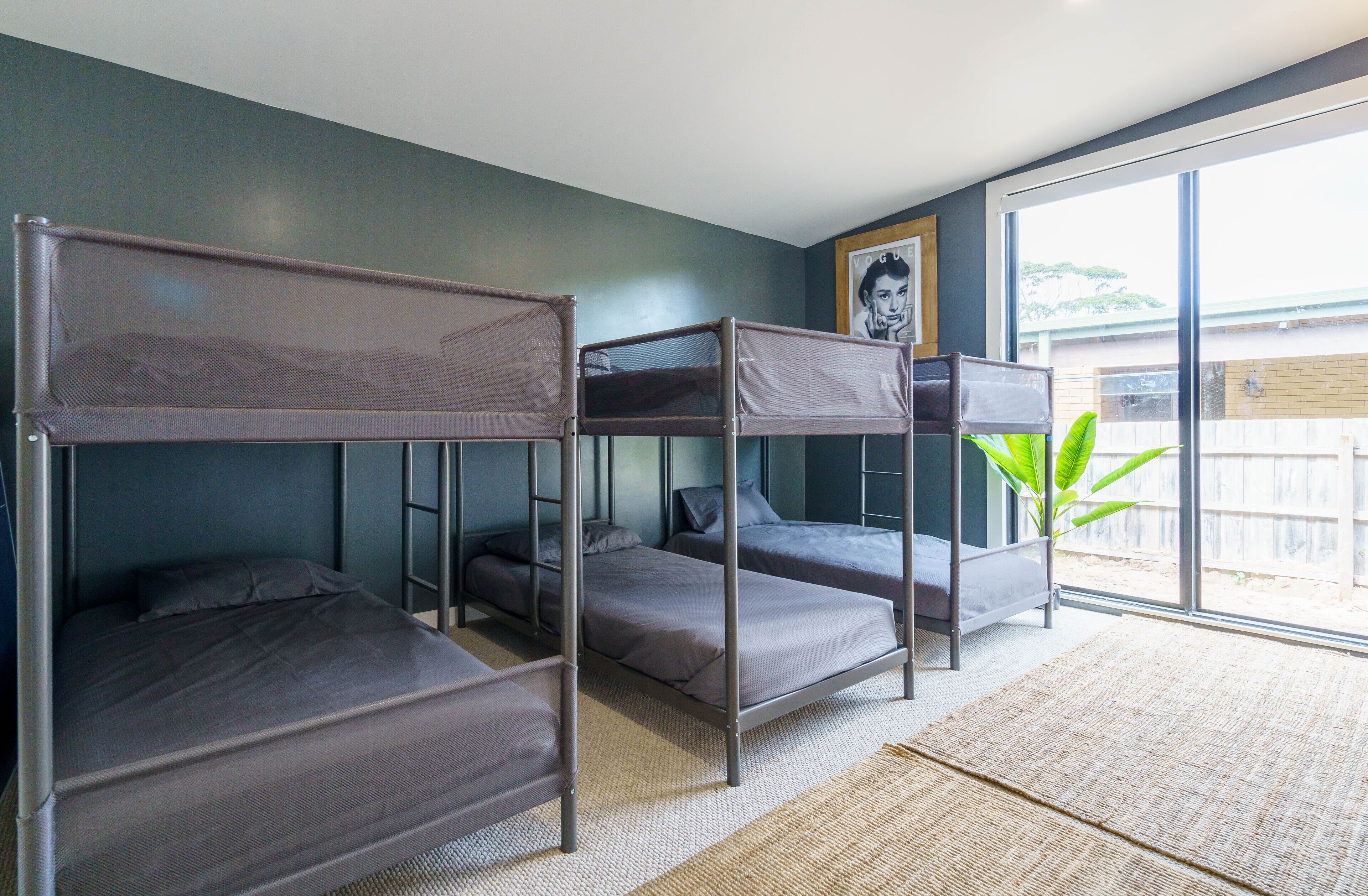 Une chambre avec des lits superposés, une grande fenêtre et un tableau encadré au mur.