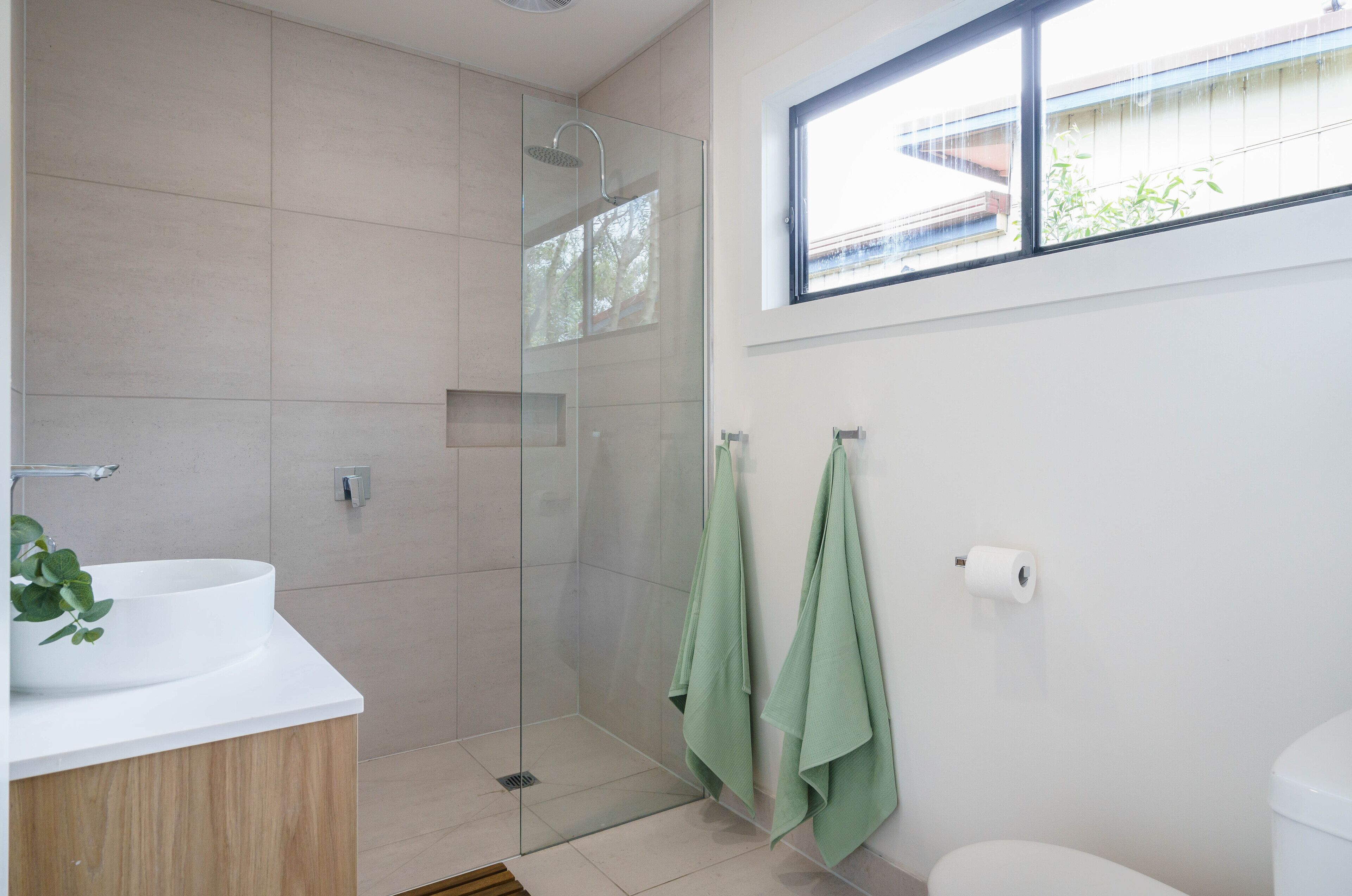 Een moderne badkamer met een douchecabine van glas, een witte wastafel en een toilet.