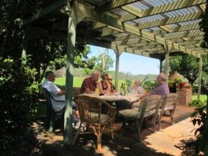 A covered outdoor seating area with a table and chairs, surrounded by greenery. - Berta's Cottage at Berry - Rural views - 3 b/r 2 bathrooms (Berry)
