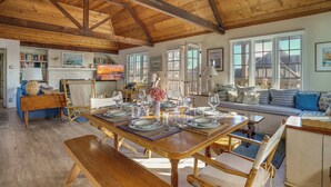 A spacious dining area with a wooden table set for a meal, a cozy seating area with a sofa and cushions, and a kitchen in the background. - Gated Fairytale Estate | Lakefront w/ Ocean Views (Oceanside)
