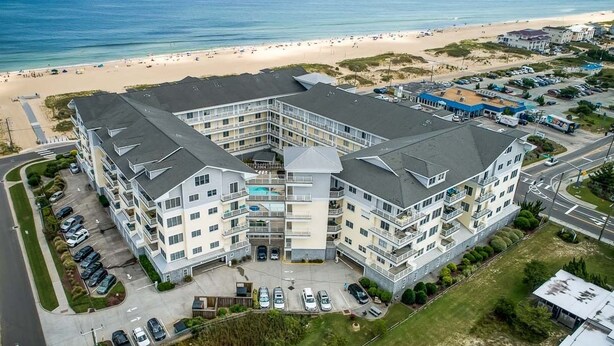 A multi-story hotel with a central courtyard, located near a beach with visible sand and ocean. - Seaside Delight | 350 ft from the beach | Community Pool (Virginia Beach)