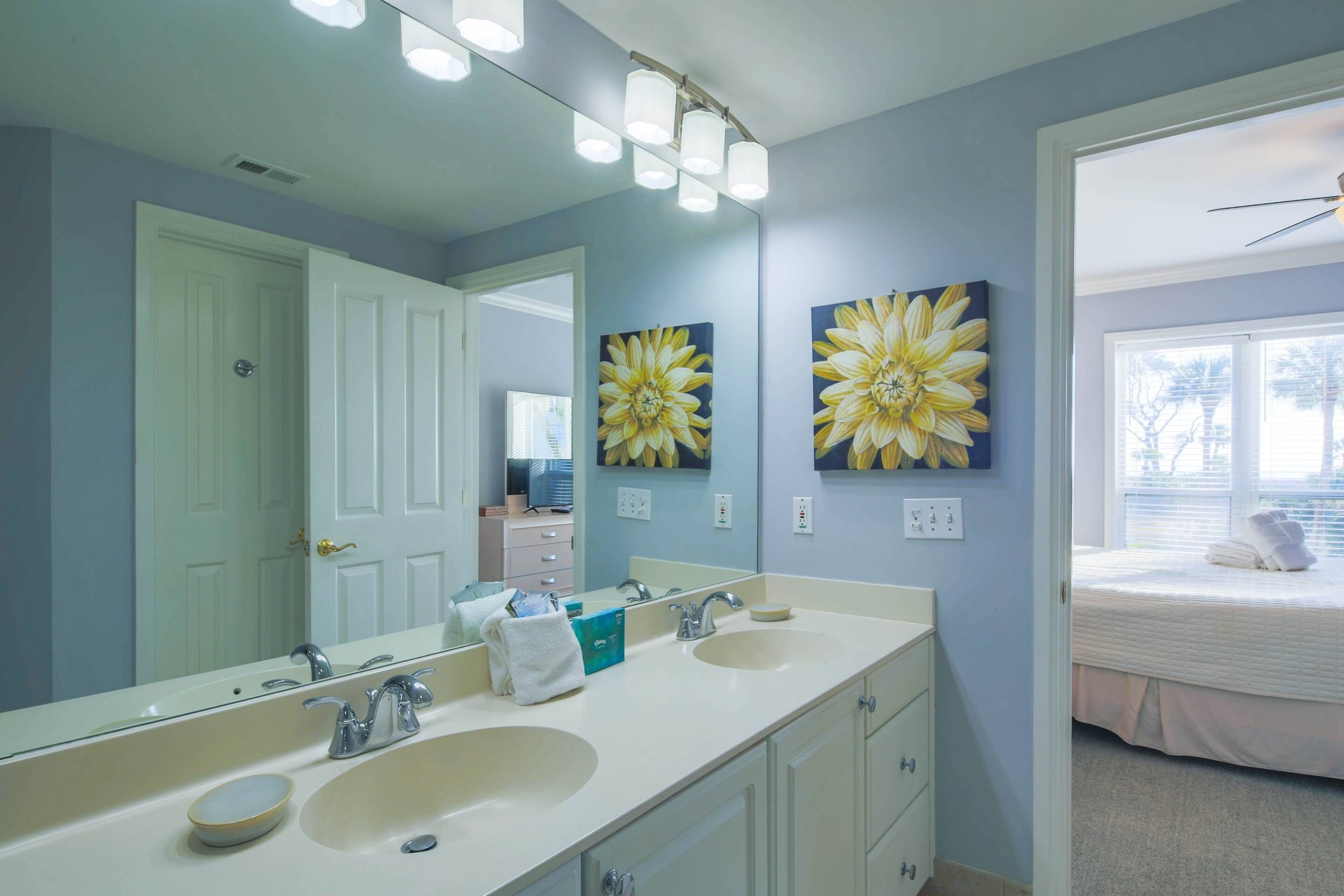 A bathroom with a double sink, a large mirror, and two wall-mounted flower paintings.