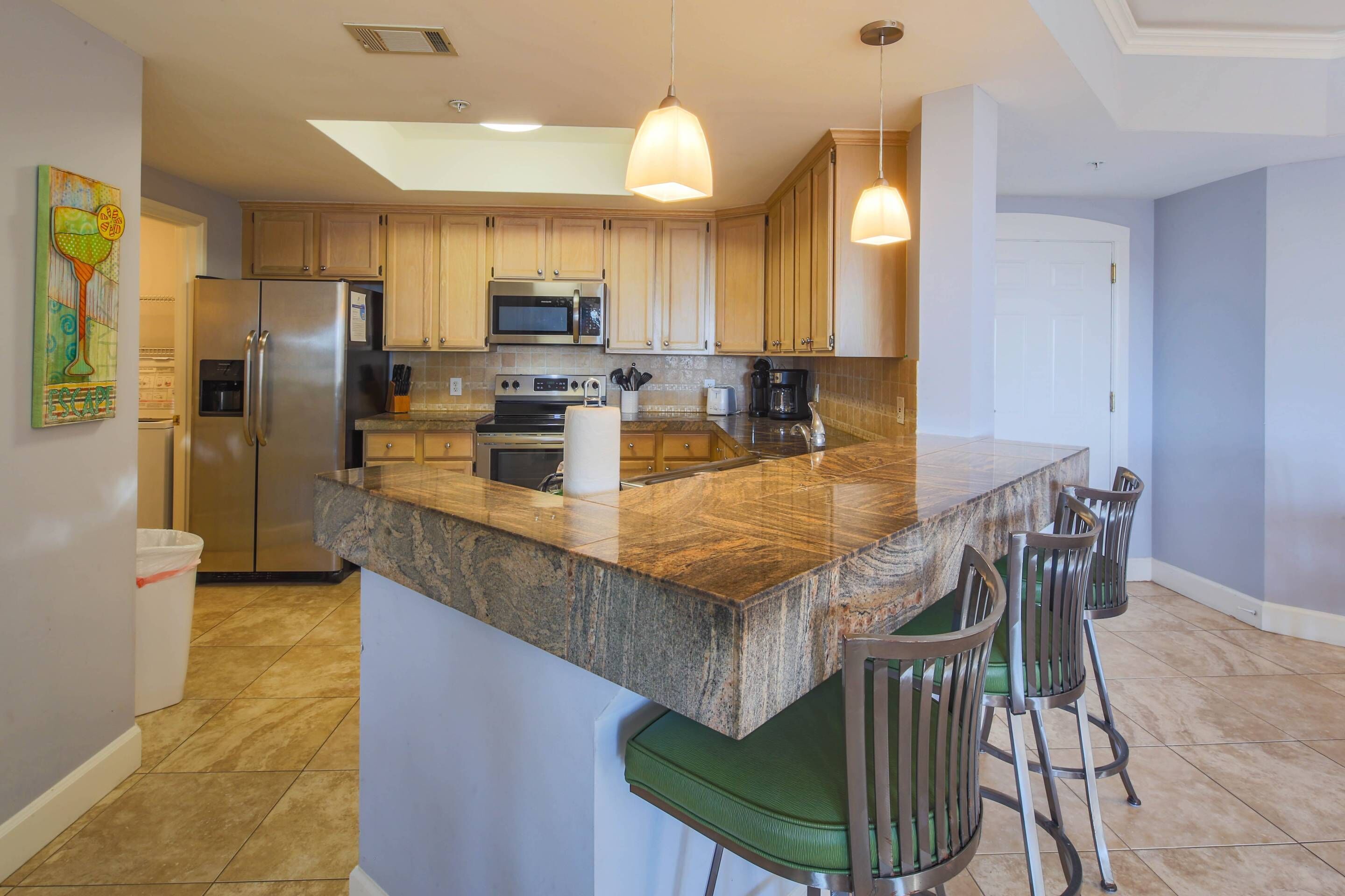 A modern kitchen with granite countertops, stainless steel appliances, and bar stools.