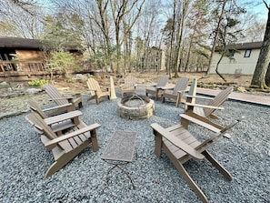 Area salotto esterna con poltrone in stile Adirondack e un braciere in pietra.