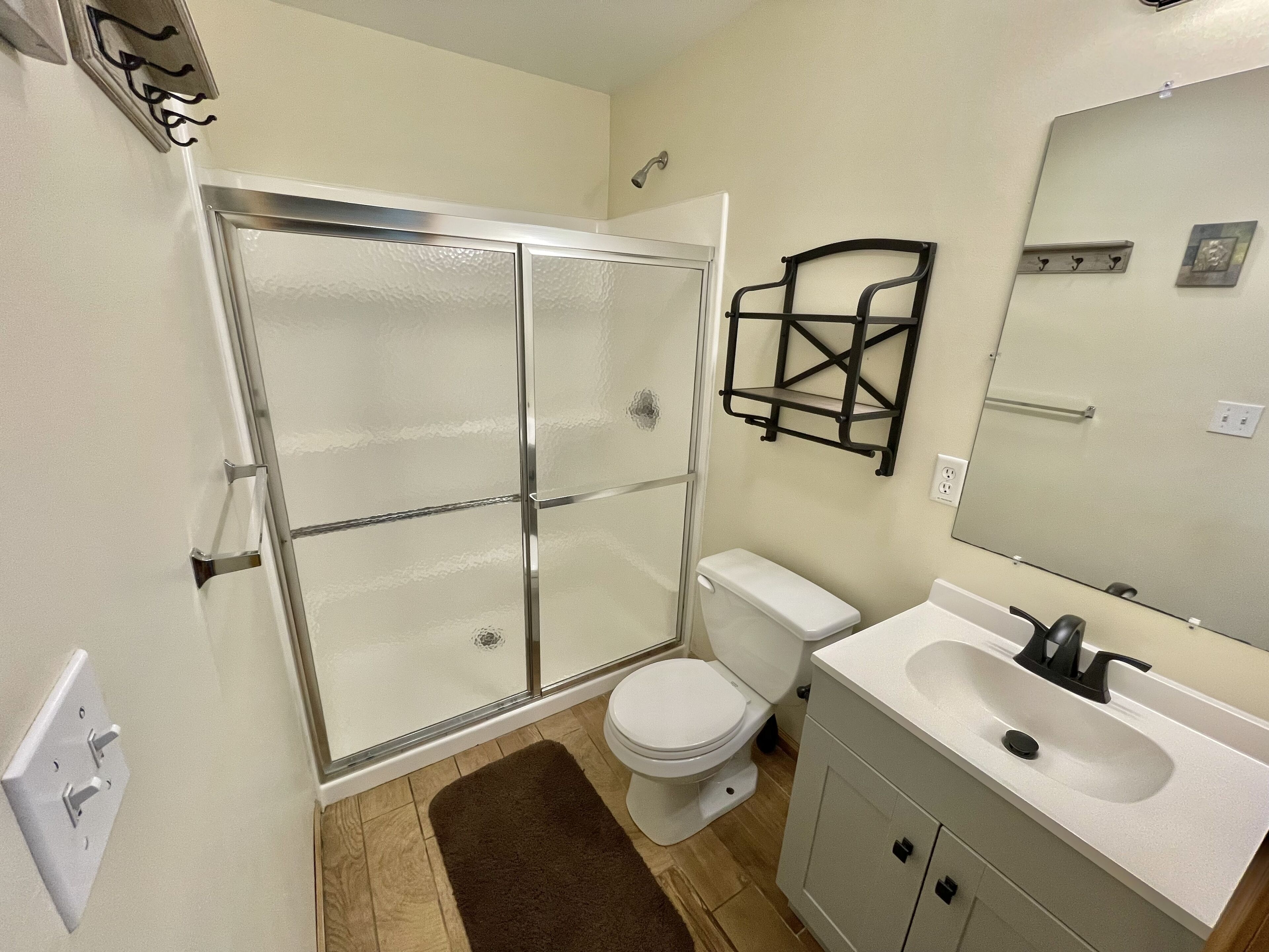 A bathroom with a glass shower enclosure, a white toilet, a sink with a mirror, and a towel rack.