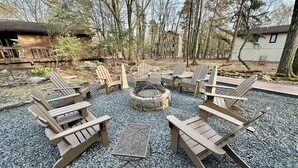 An outdoor seating area with Adirondack chairs arranged around a stone fire pit. - Four Seasons Vacation Home By Lake,  HOT TUB, WIFI,BEACH passes, Canoe, FIRE PIT (Lake Harmony)