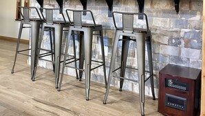 A bar area with four metal bar stools, a flat-screen TV mounted above, and a stone accent wall. - Four Seasons Vacation Home By Lake,  HOT TUB, WIFI,BEACH passes, Canoe, FIRE PIT (Lake Harmony)